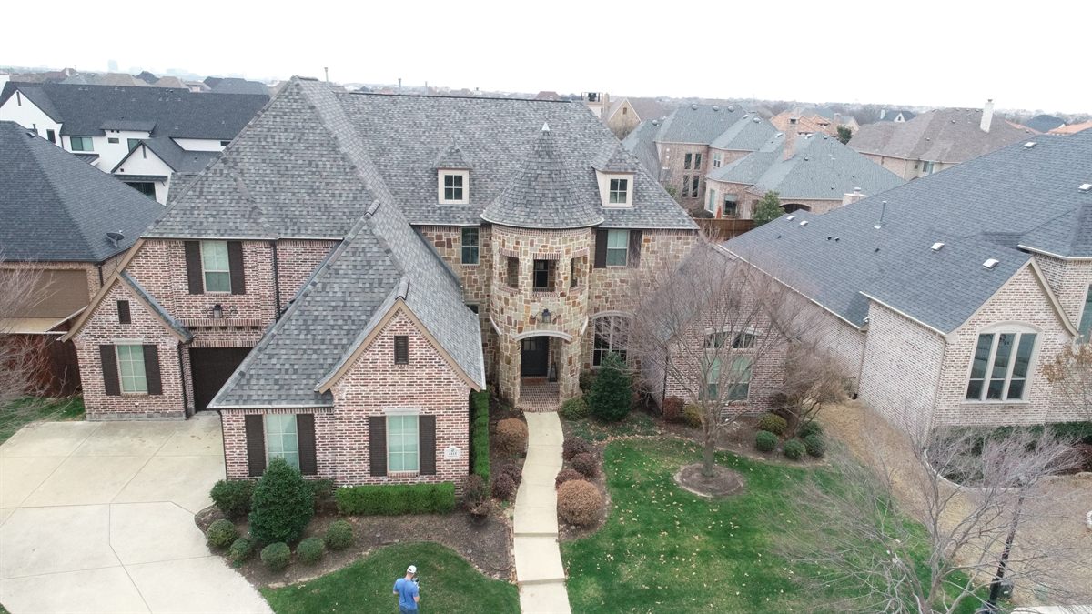 Aerial view of a large stone-and-brick home with a newly installed architectural shingle roof in Frisco