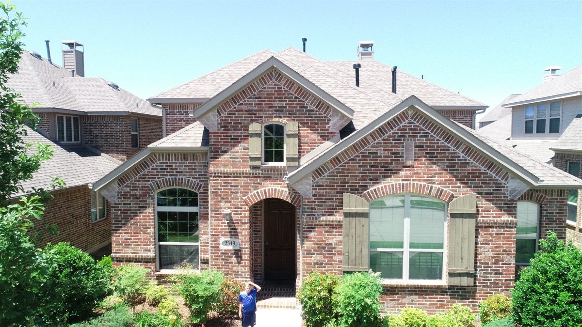 Aerial front view of a brick two-story Plano home with new architectural shingles