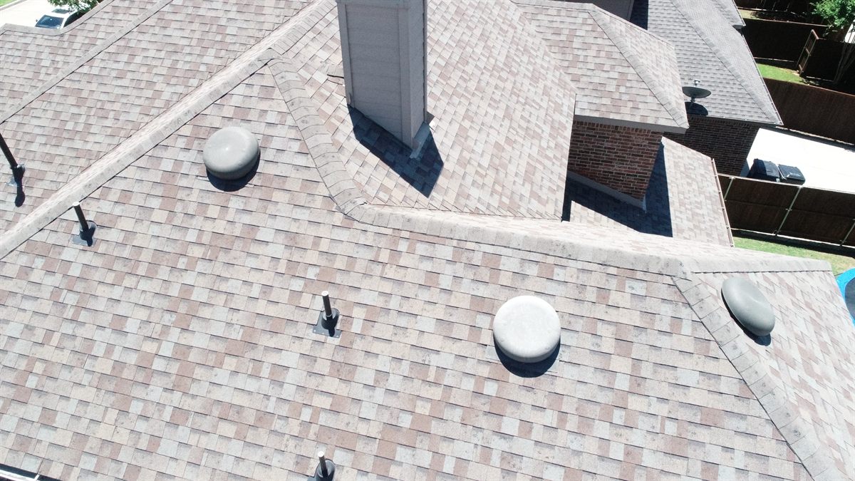 Aerial view of a freshly completed architectural shingle roof with vents and chimney in Allen