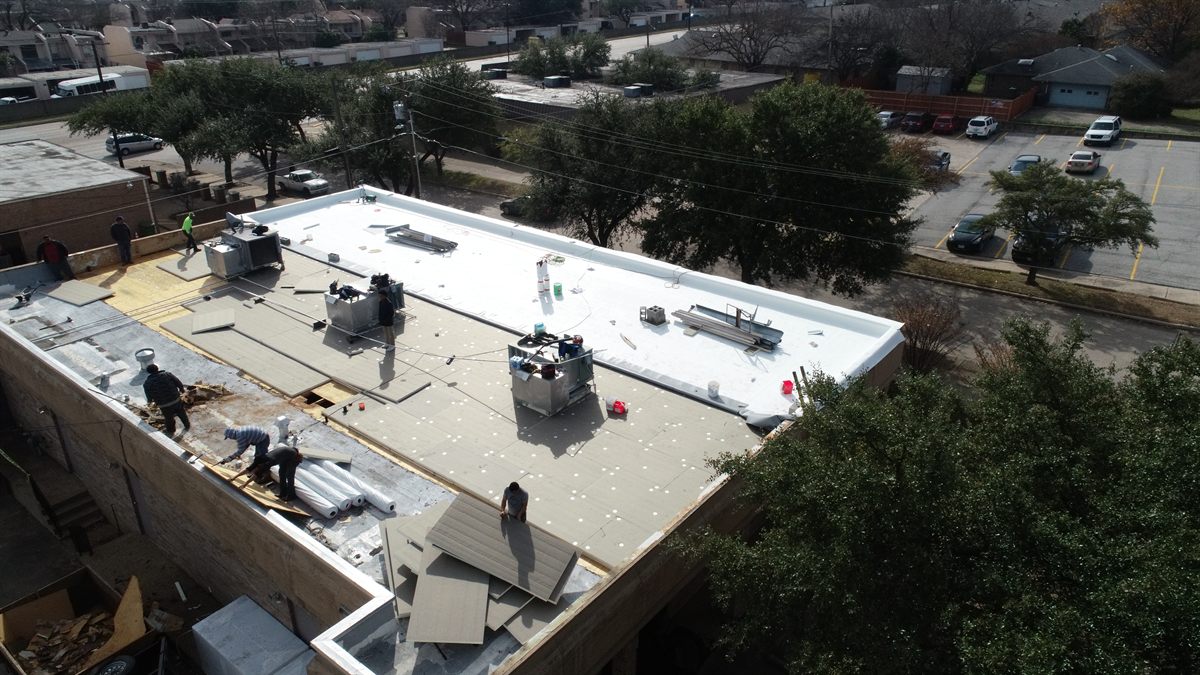 Aerial drone view of a commercial flat-roof installation in progress in Fort Worth — crews placing TPO membrane
