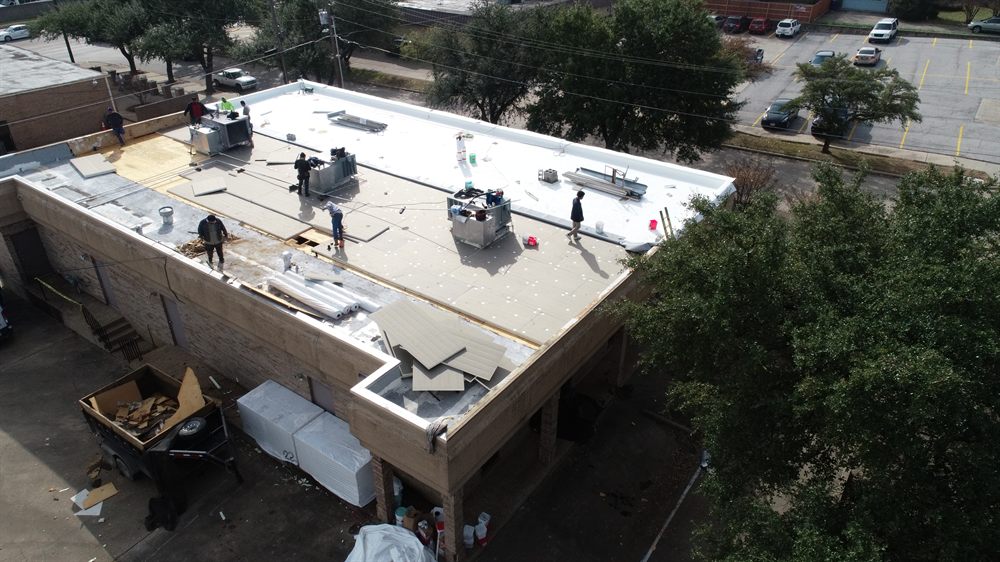 Aerial view of a Top Hat Roofing crew installing a TPO single-ply membrane on a commercial flat roof in DFW