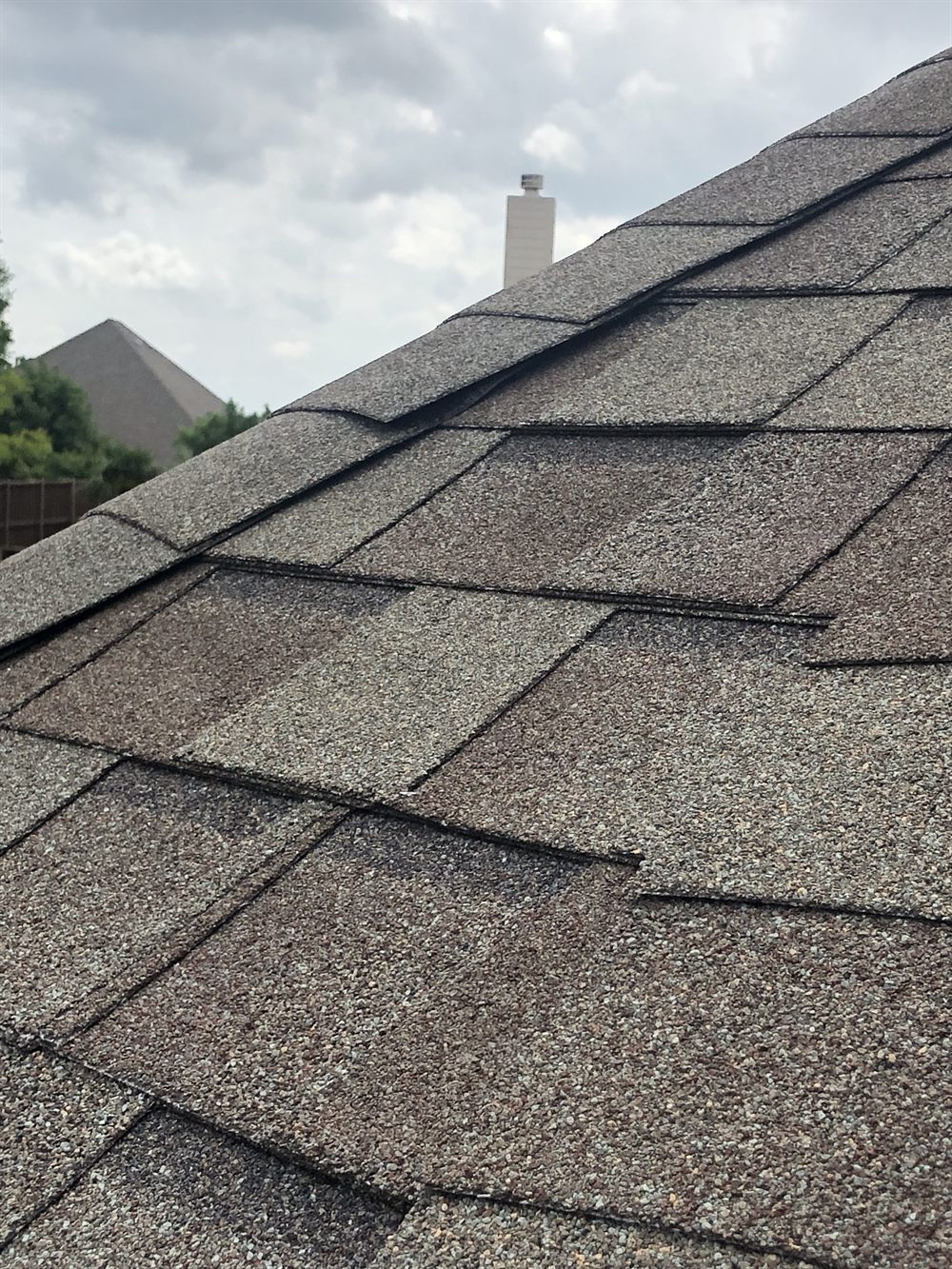Repaired roof ridge with new architectural shingles and chimney flashing on a Plano home